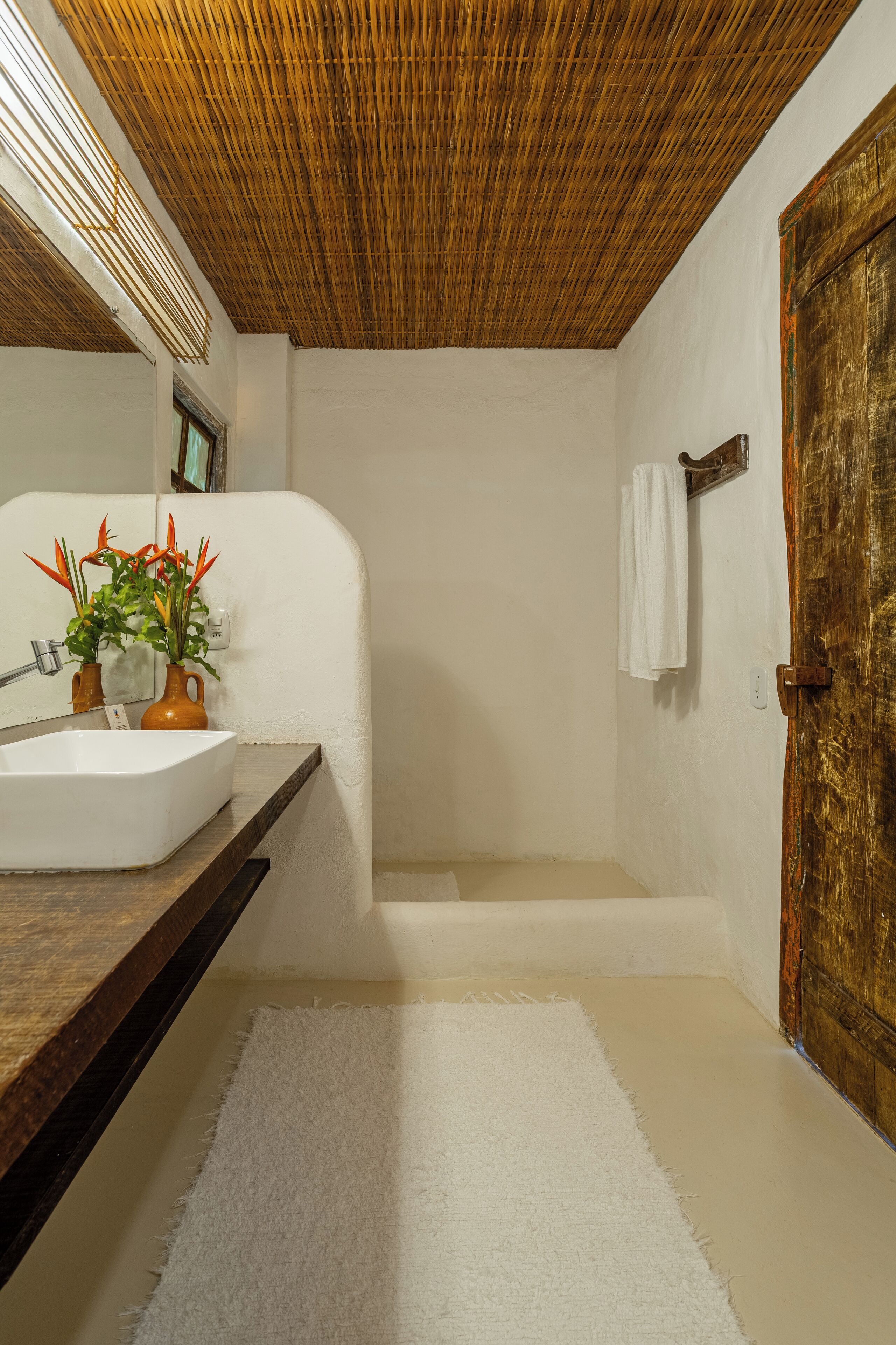 A bathroom with a white sink, a wooden countertop, a mirror, a shower area, and a wooden door.