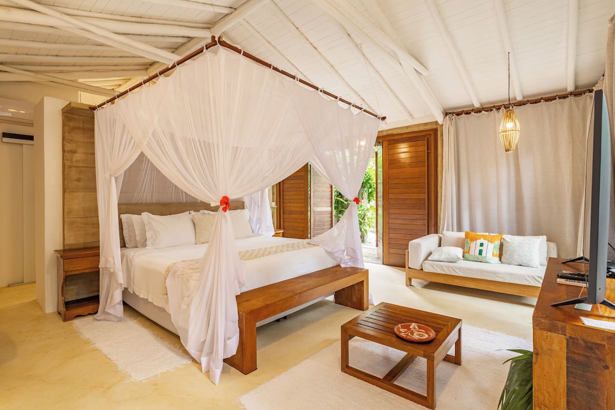 Un dormitorio con una cama con dosel, un banco de madera, un sofá y un escritorio con un ordenador.
