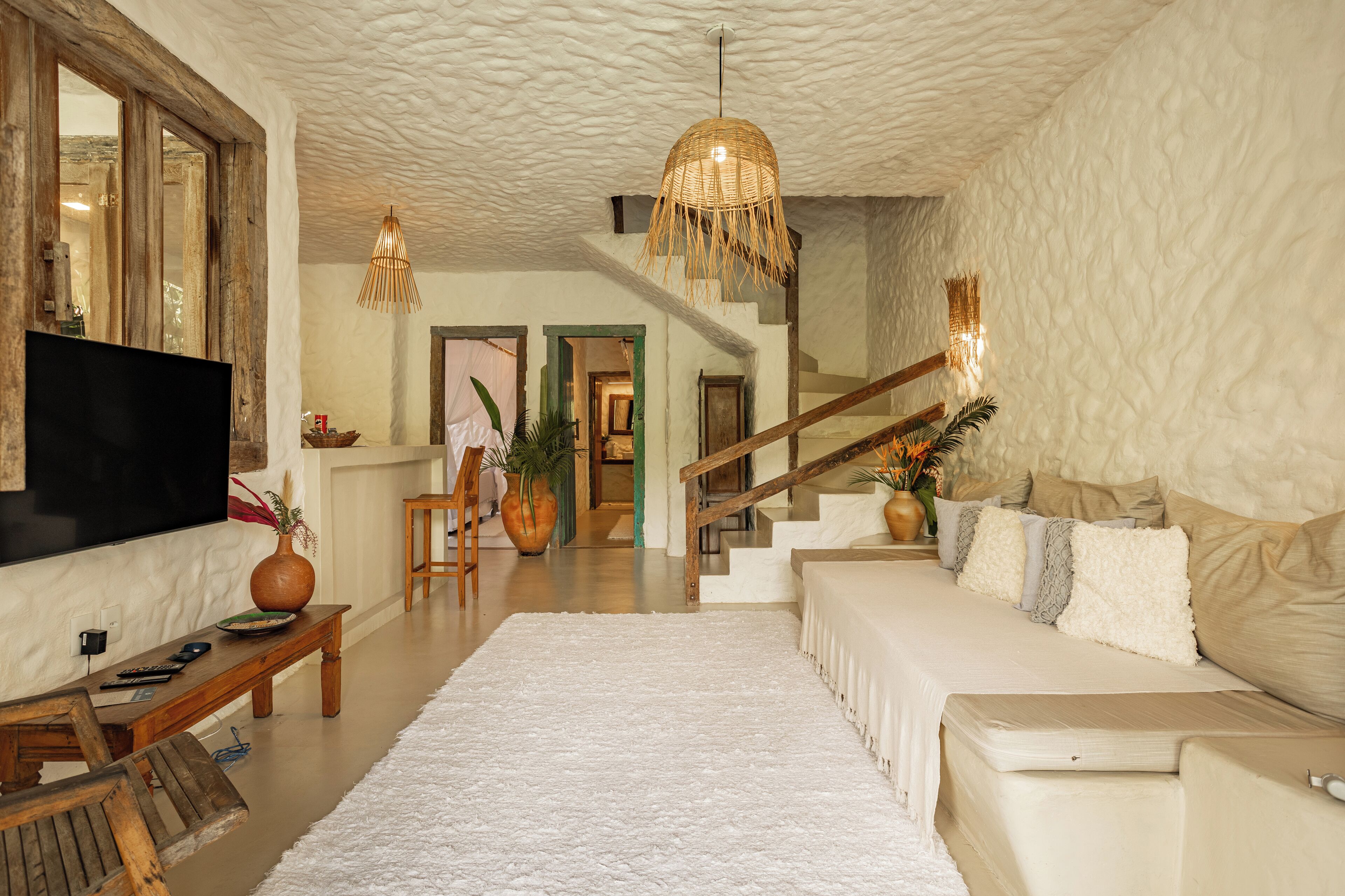 A spacious living room with a large flat-screen TV, a wooden coffee table, a white sofa, and a staircase leading to another level.