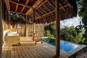 A wooden deck with a thatched roof, a pool, and lush greenery in the background. - Hotel Boutique Bahia Bonita (Porto Seguro)