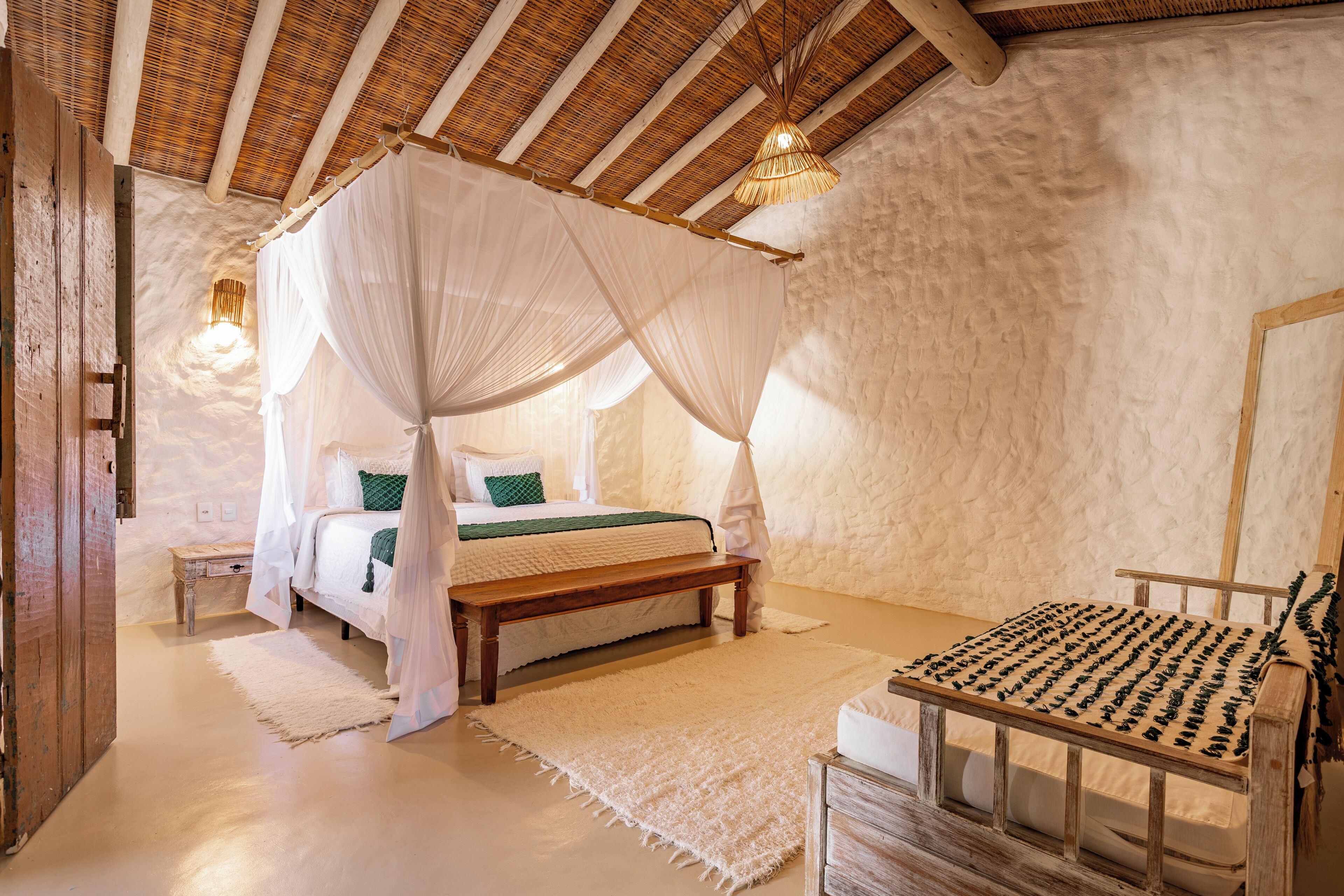 Ein Schlafzimmer mit einem Himmelbett, einer hölzernen Bank und einer gewebten Decke.