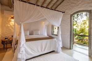 A bedroom with a four-poster bed, a bedside table, and a view of greenery through a window. - Hotel Boutique Bahia Bonita (Porto Seguro)