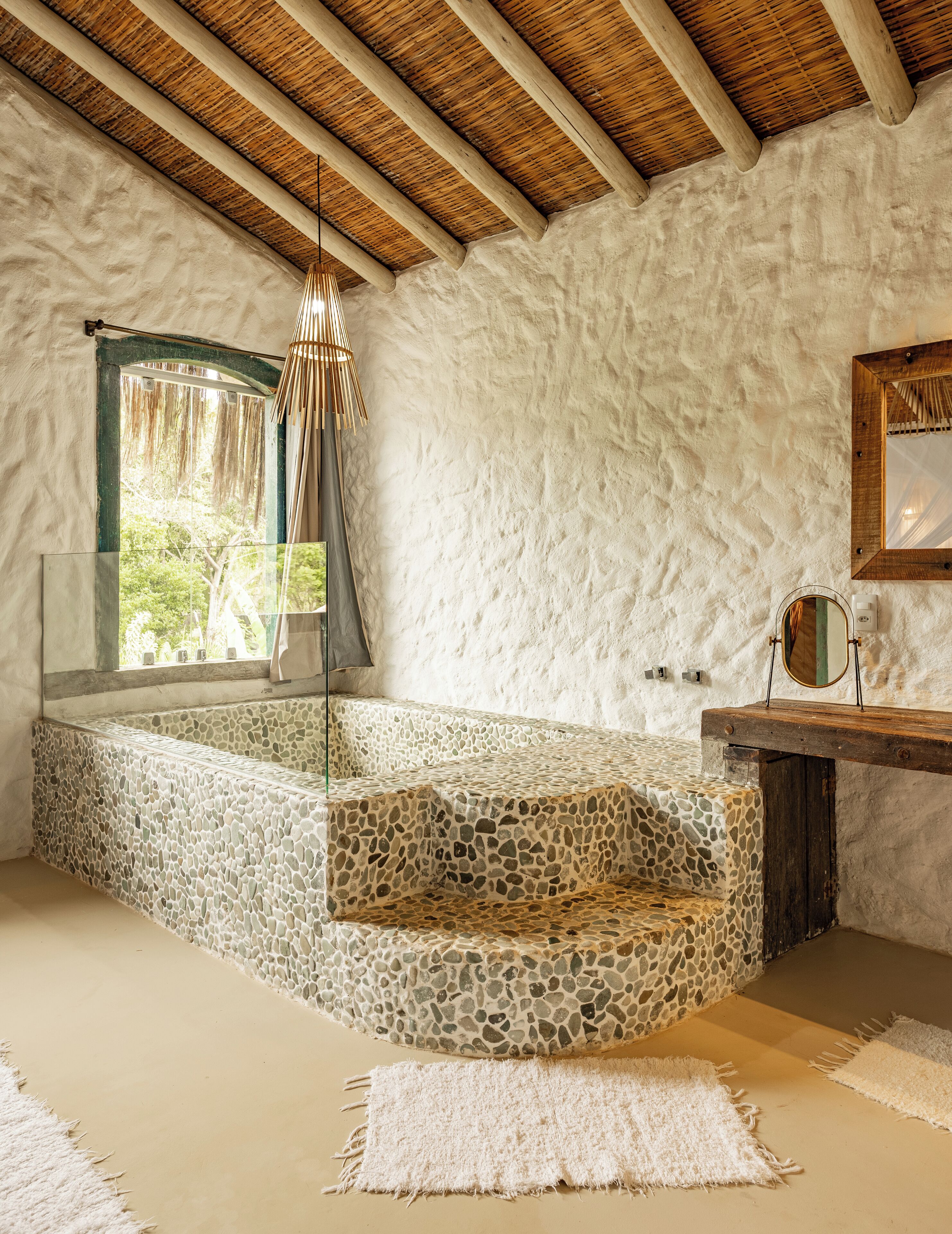A bathroom with a stone mosaic floor, a wooden bench, a mirror, and a hanging light fixture.