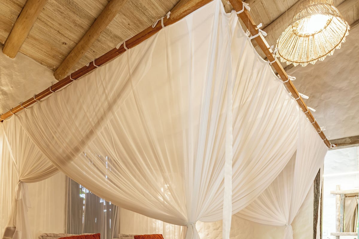 Un dormitorio con cama con dosel, ropa de cama blanca y techo de madera.