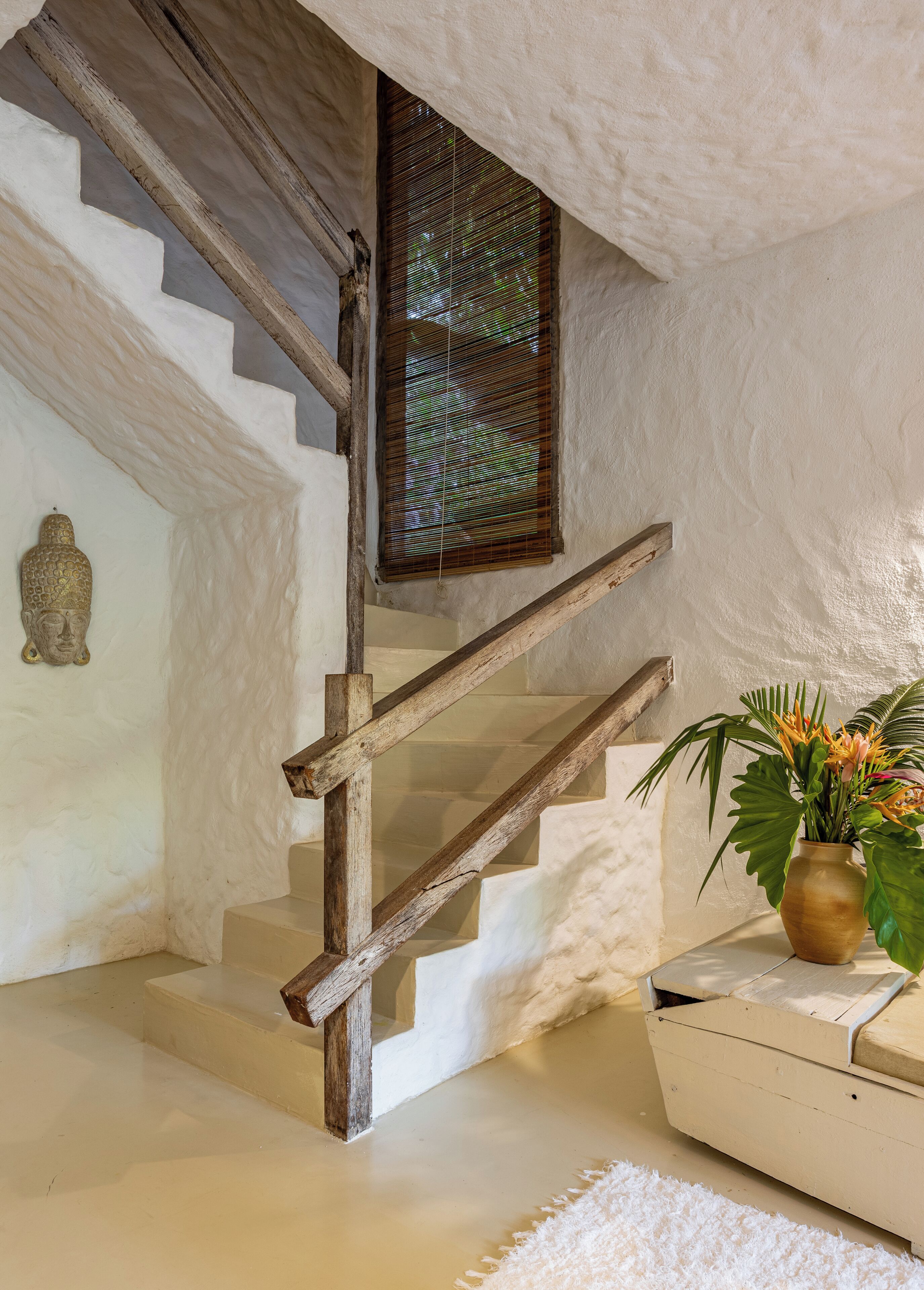A staircase with wooden steps and a wooden handrail, leading to a room with a white wall and a window with blinds.