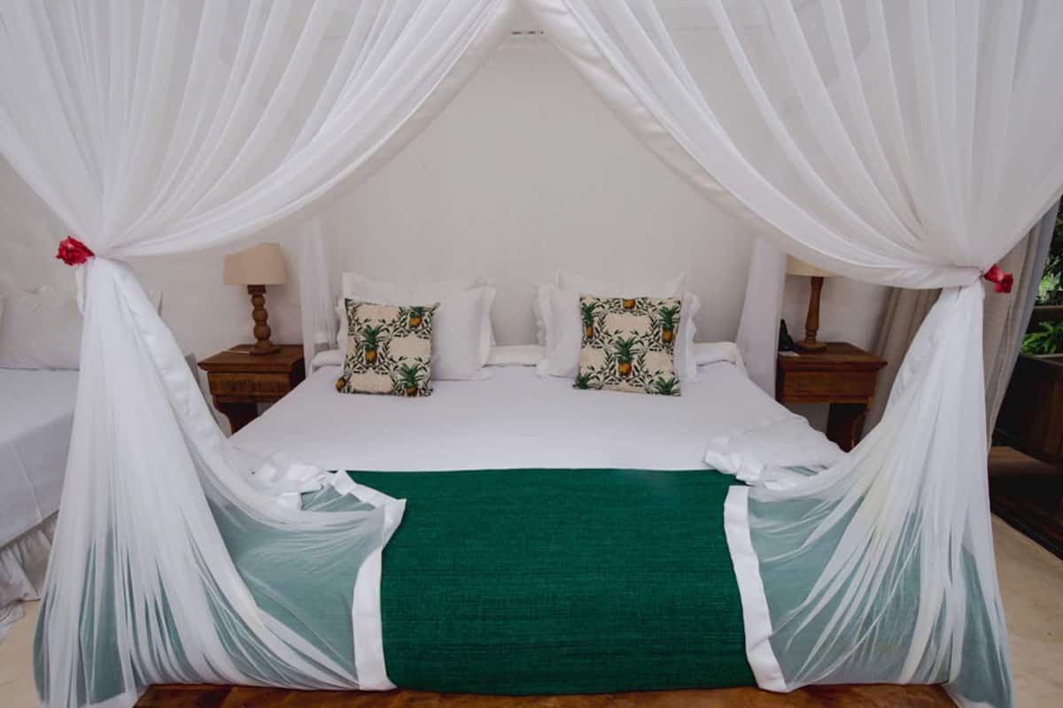 Una cama con dosel, dos mesitas de noche y dos almohadas con estampado tropical.