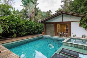 A swimming pool with a wooden deck, a small hot tub, and a building with a sliding door. - Hotel Boutique Bahia Bonita (Porto Seguro)