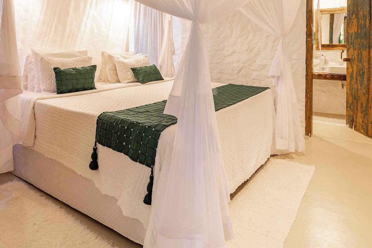 Un dormitorio con cama con dosel, alfombra blanca y puerta de madera.