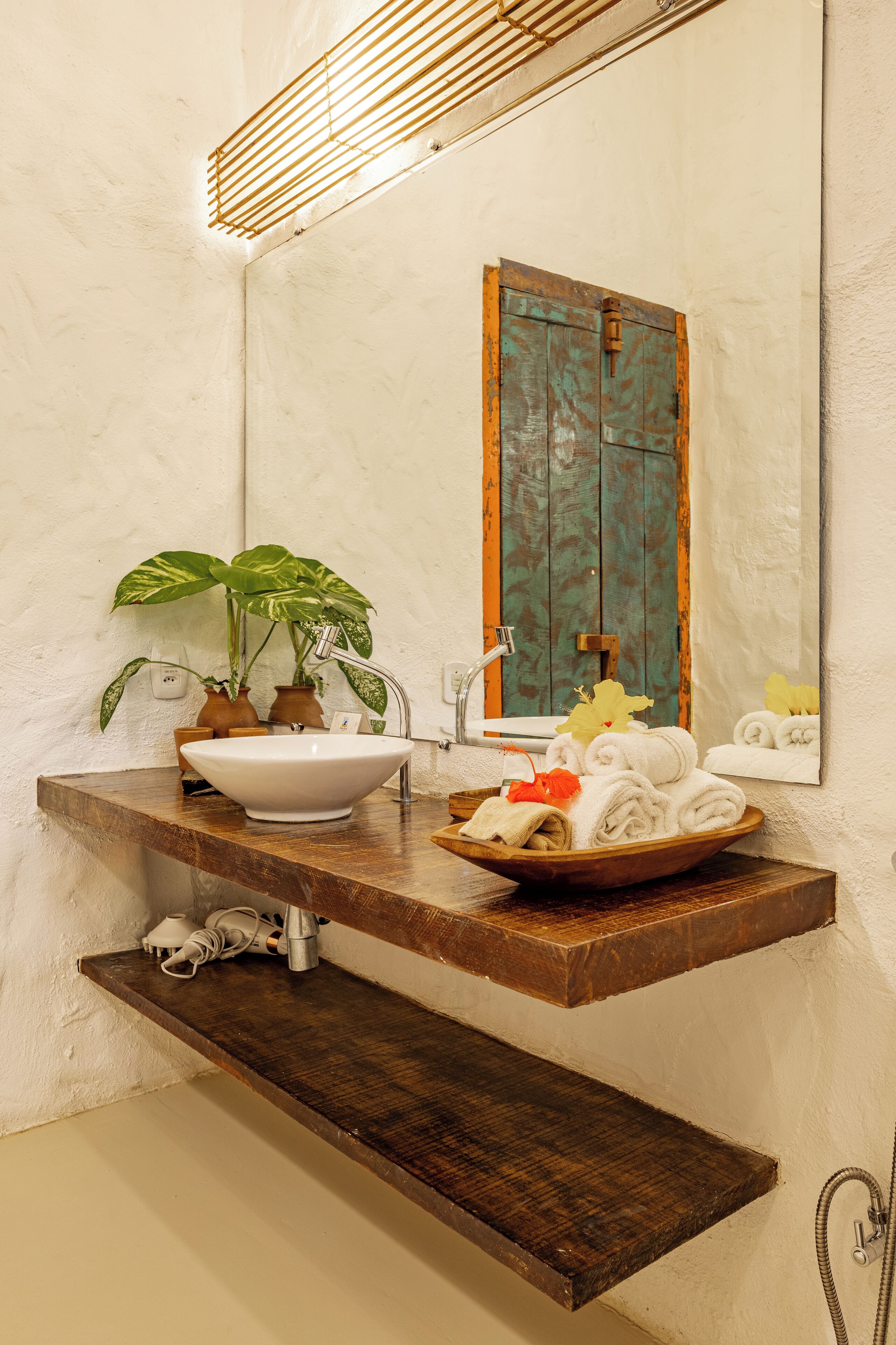A bathroom with a wooden vanity, a white sink, a mirror, and a potted plant.