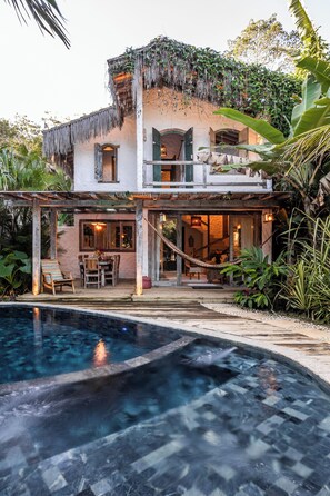 Una casa con piscina, un patio cubierto y exuberante vegetación.