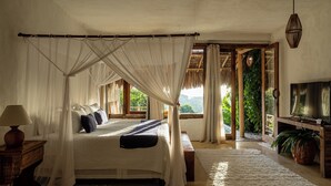 A bedroom with a canopy bed, a television, and a view of greenery outside. - Hotel Boutique Bahia Bonita (Porto Seguro)