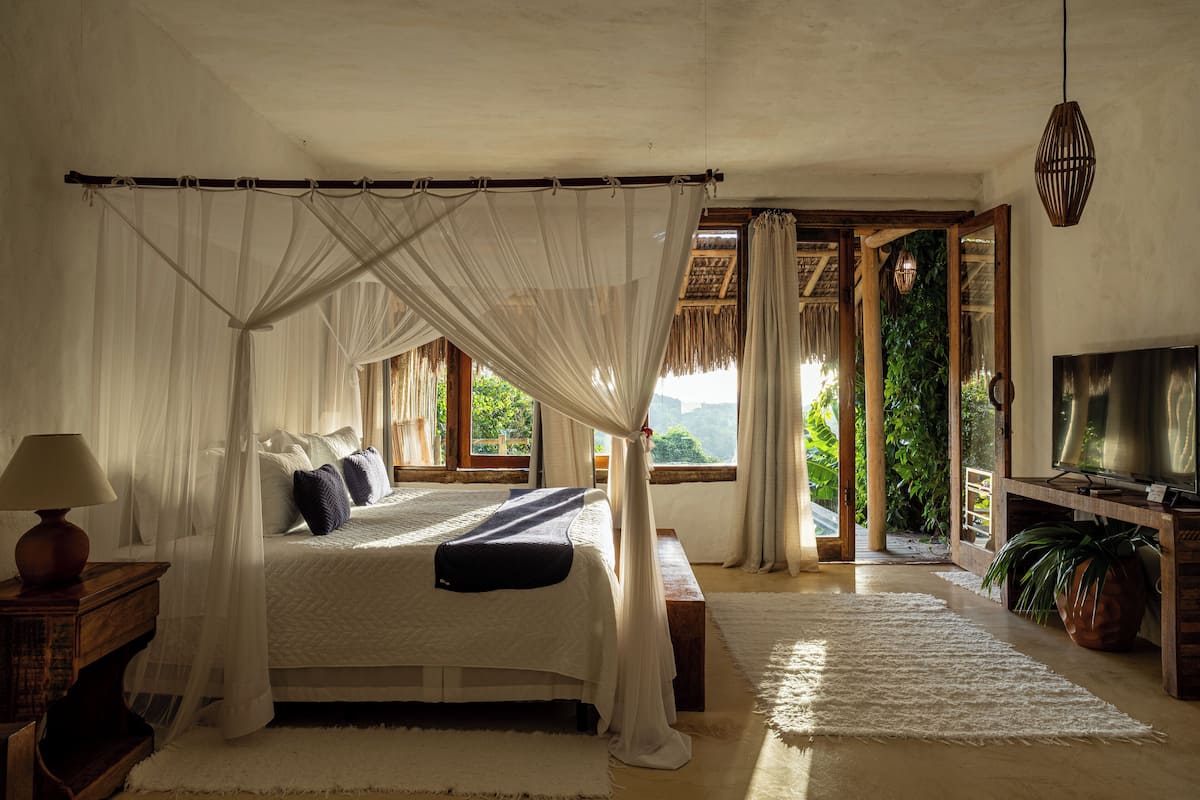Un dormitorio con cama con dosel, televisor y vistas al exterior a zonas verdes.