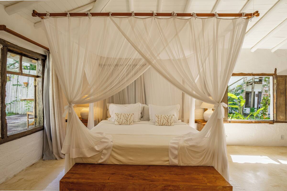 Una cama con dosel, cabecera de madera, mesitas de noche y vistas a zonas verdes.