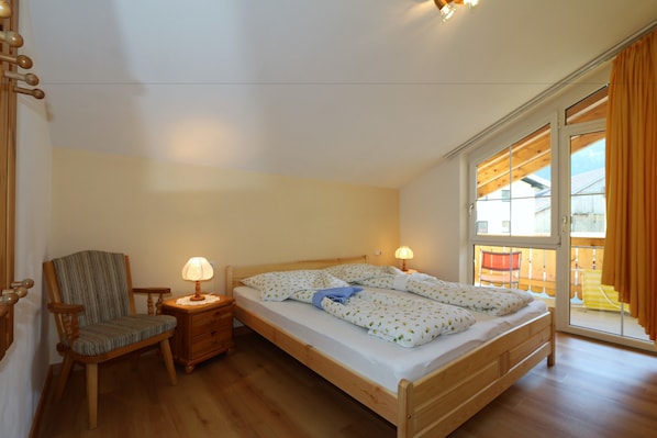 A bedroom with a wooden bed, a chair, a nightstand, and a window with curtains.