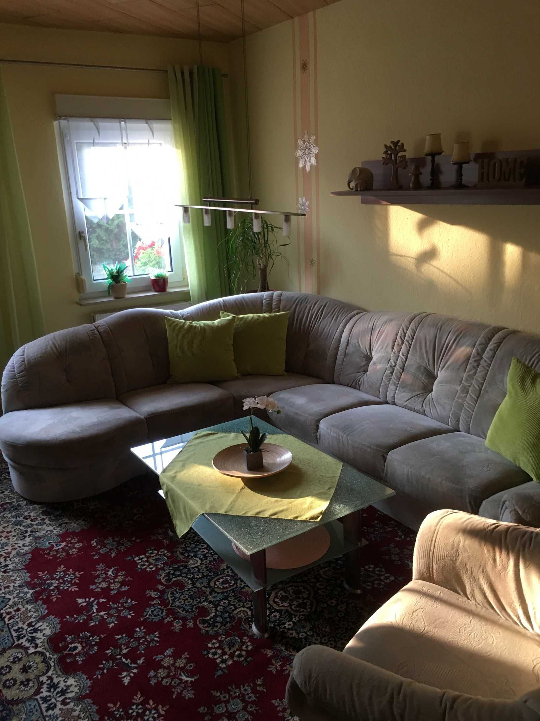 Un salon avec un grand canapé en forme de L, une table basse ornée d’un plateau décoratif, un tapis à motifs et une fenêtre avec des rideaux.
