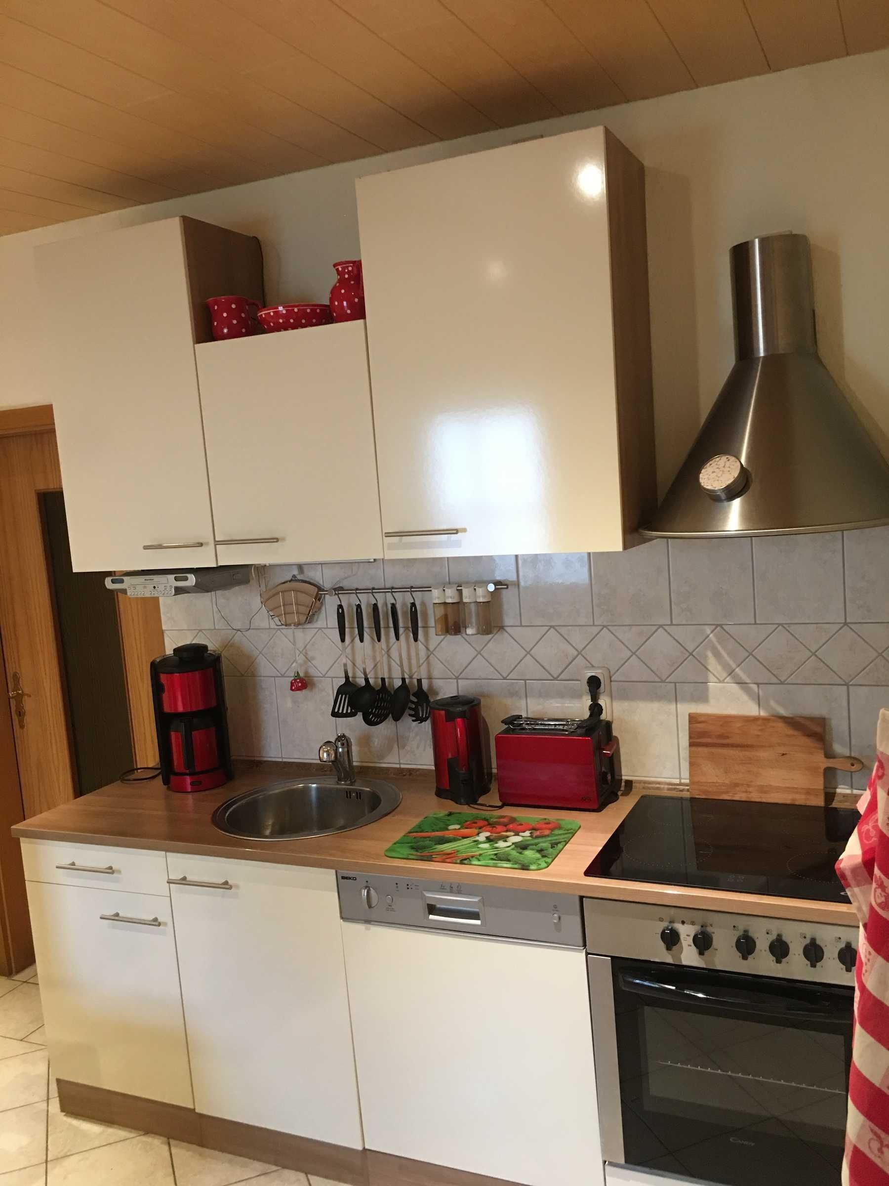 A kitchen with white cabinets, a stainless steel range hood, a dishwasher, a stove, and various kitchen utensils.