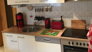 A kitchen with white cabinets, a stainless steel range hood, a dishwasher, a stove, and various kitchen utensils.