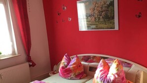 A bedroom with a bed, a window with red curtains, a radiator, and a painting on the wall.
