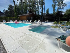 Una piscina con múltiples sillas de descanso y una pequeña casa al fondo.