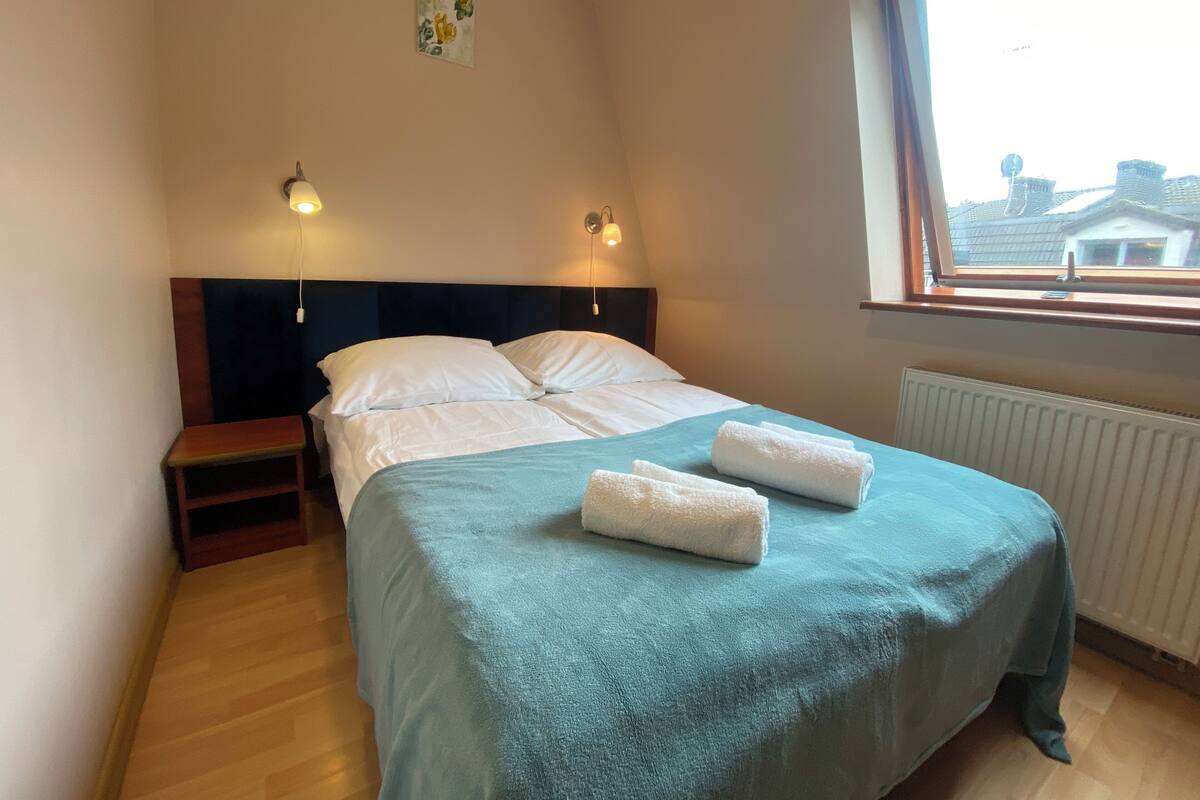 Ein Schlafzimmer mit einem Bett, zwei Nachttischen, einem Fenster und einer Heizung.