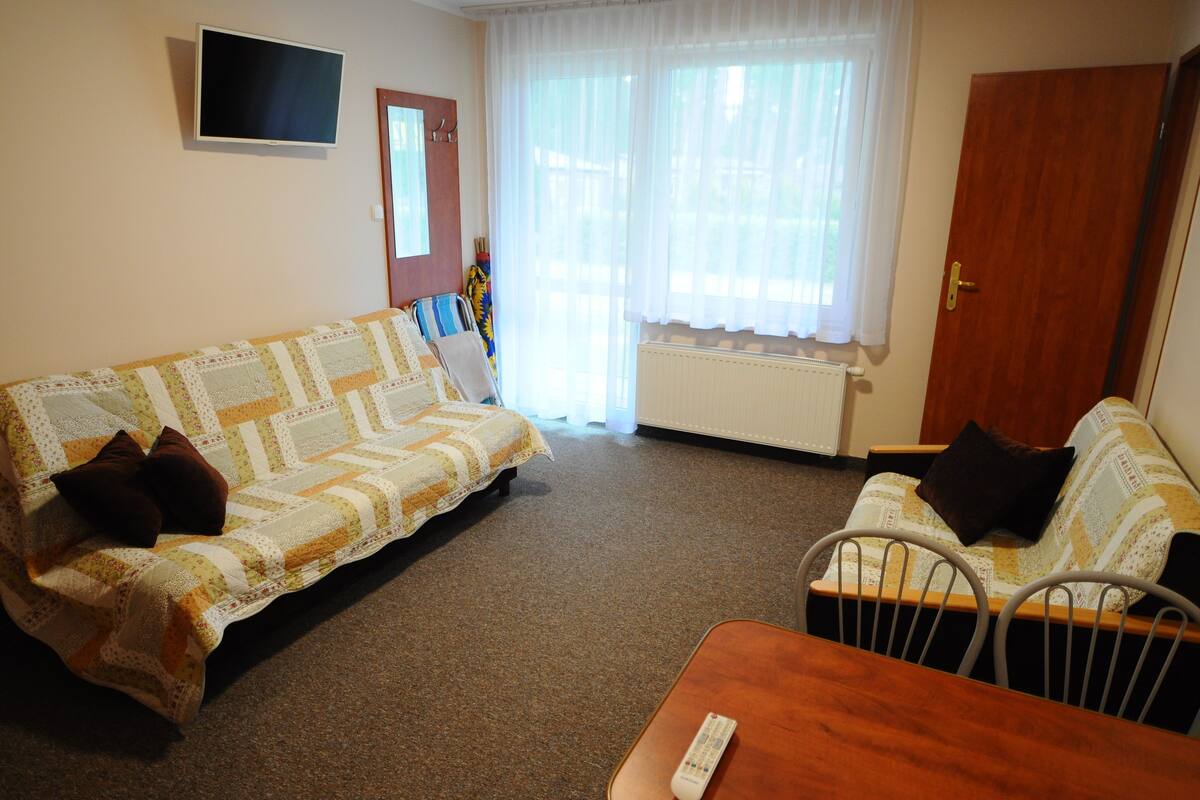 Ein Wohnzimmer mit zwei Sofas, einem Fernseher und einem Fenster mit Vorhängen.