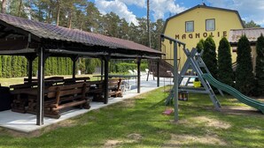En park med picnicborde, et legeplads og en gul bygning med teksten "MAGNOLIE".