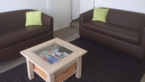 A living room with two brown leather sofas, each with a green pillow, and a glass-top coffee table with a woven basket underneath.