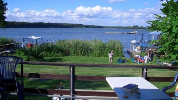 A lakeside patio with a table and chairs, a grassy area, and a dock with boats.