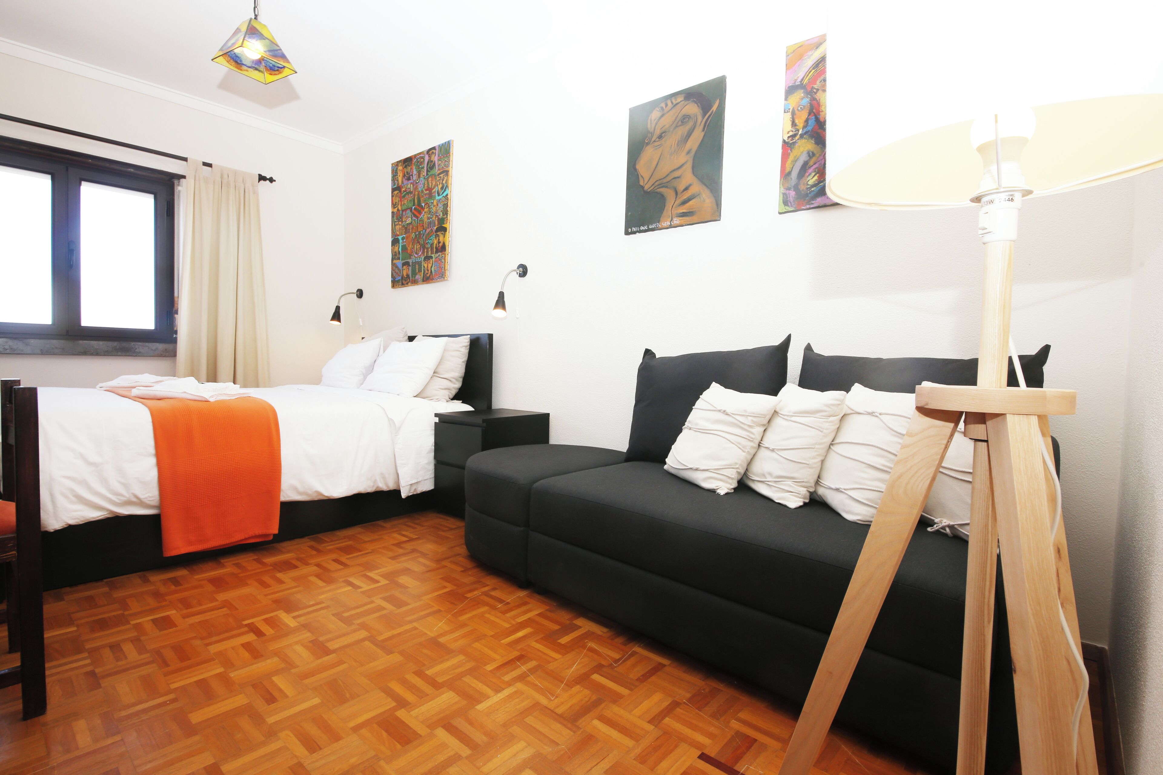 Una habitación con cama, sofá, lámpara y obras de arte en las paredes.
