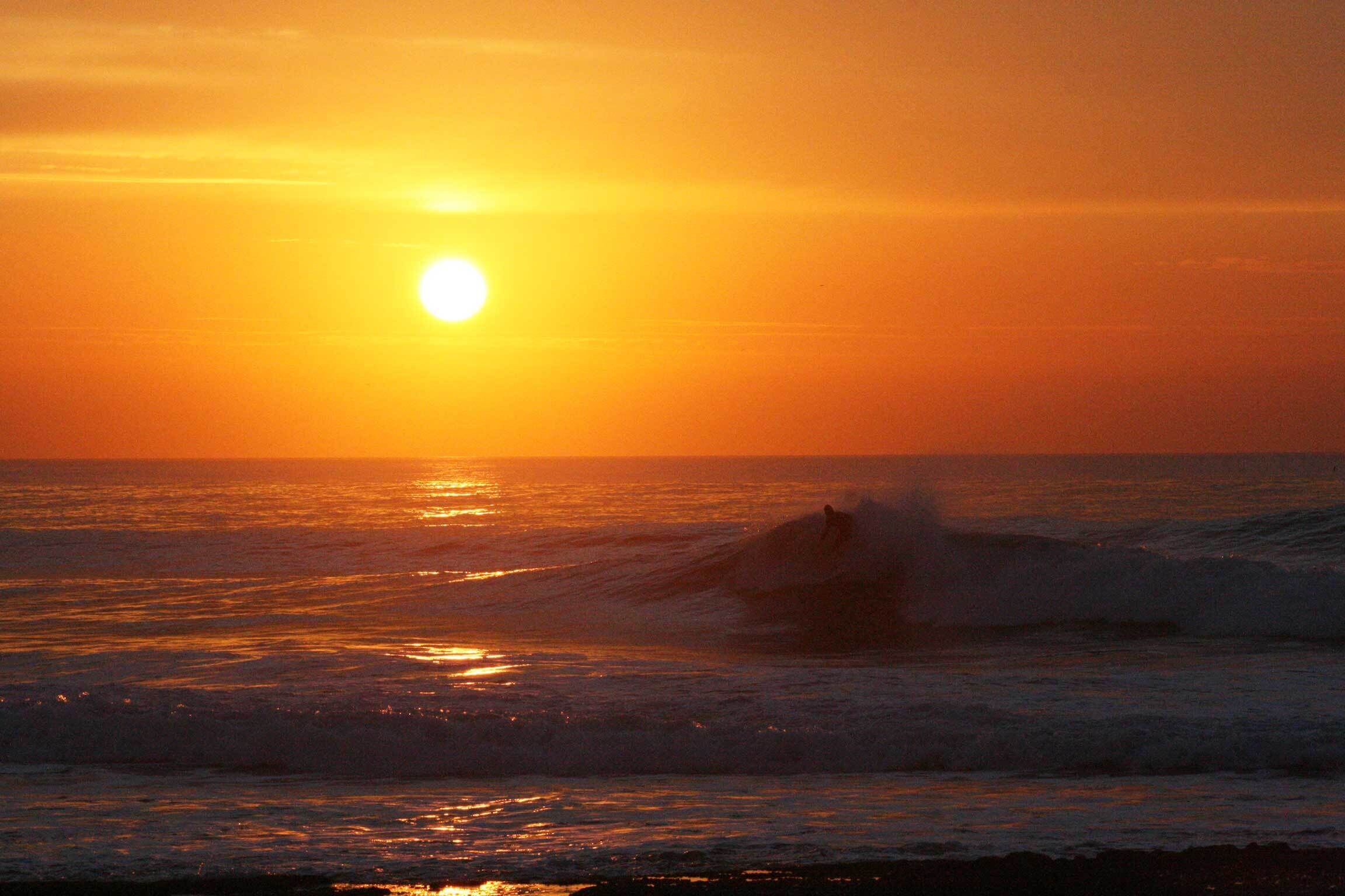Un coucher de soleil sur l’océan, avec des vagues.