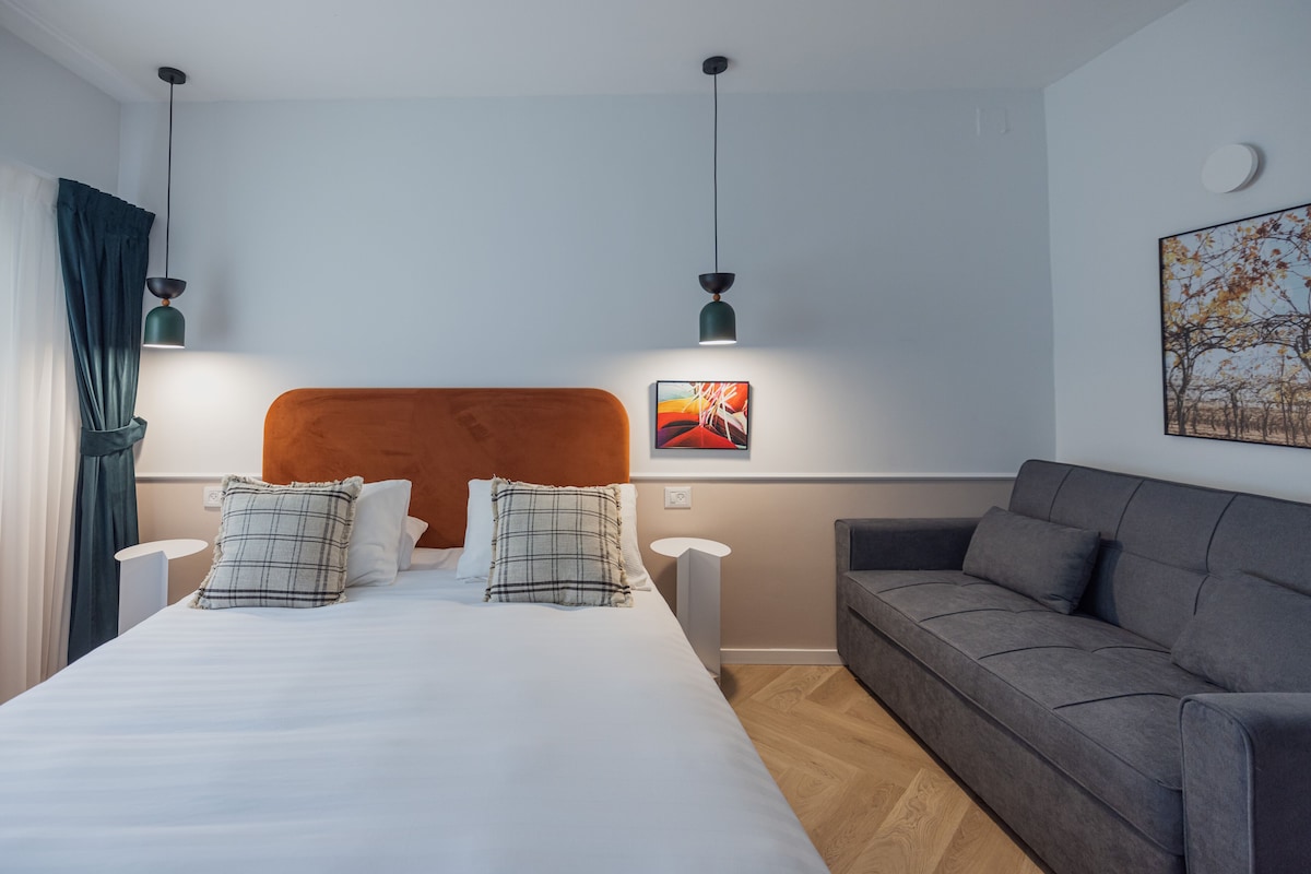 Um quarto moderno com uma cama grande, um sofá cinzento e duas luminárias pendentes.