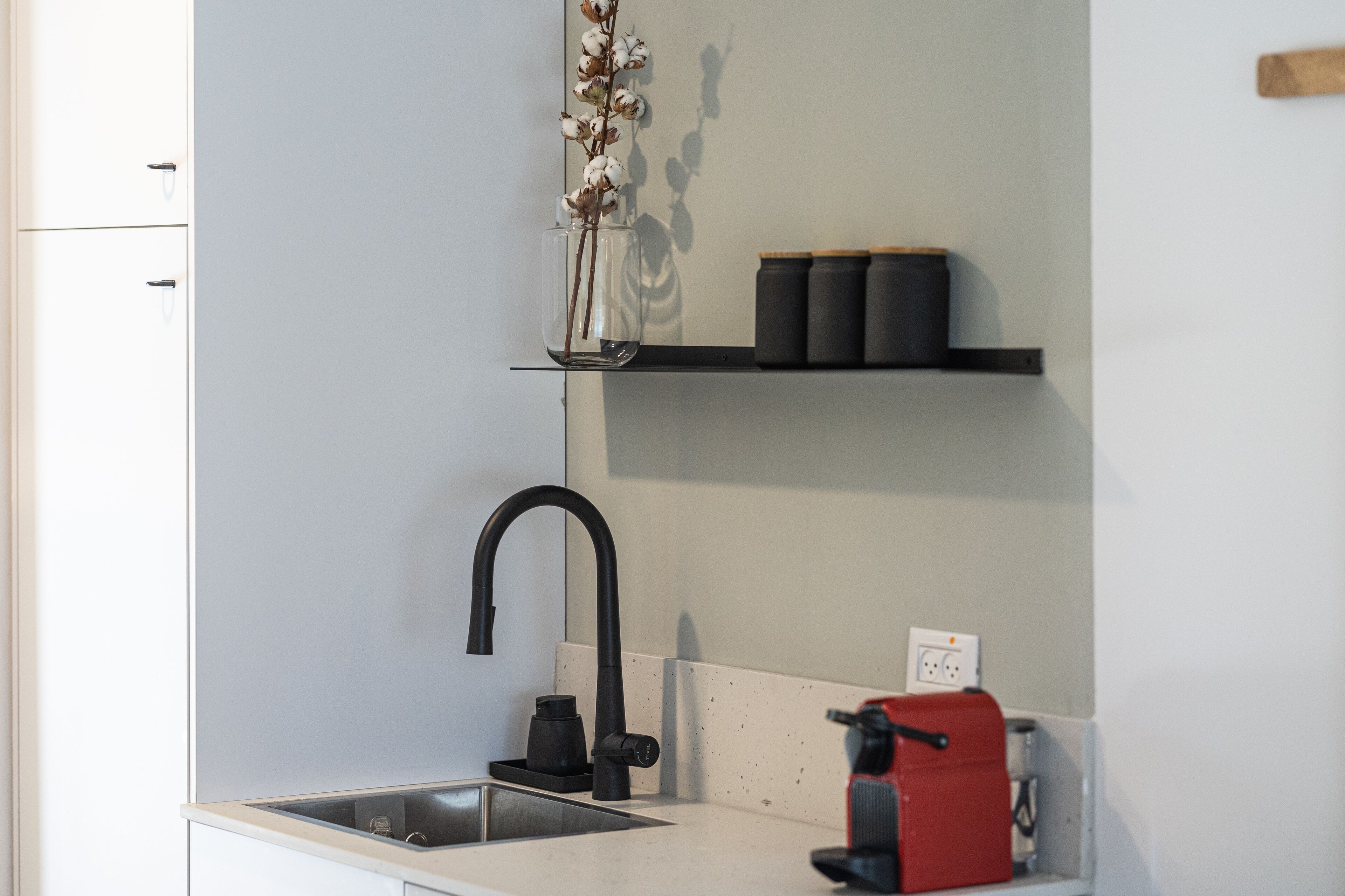 A modern kitchen with a black faucet, a coffee machine, and a vase with dried flowers on the countertop.