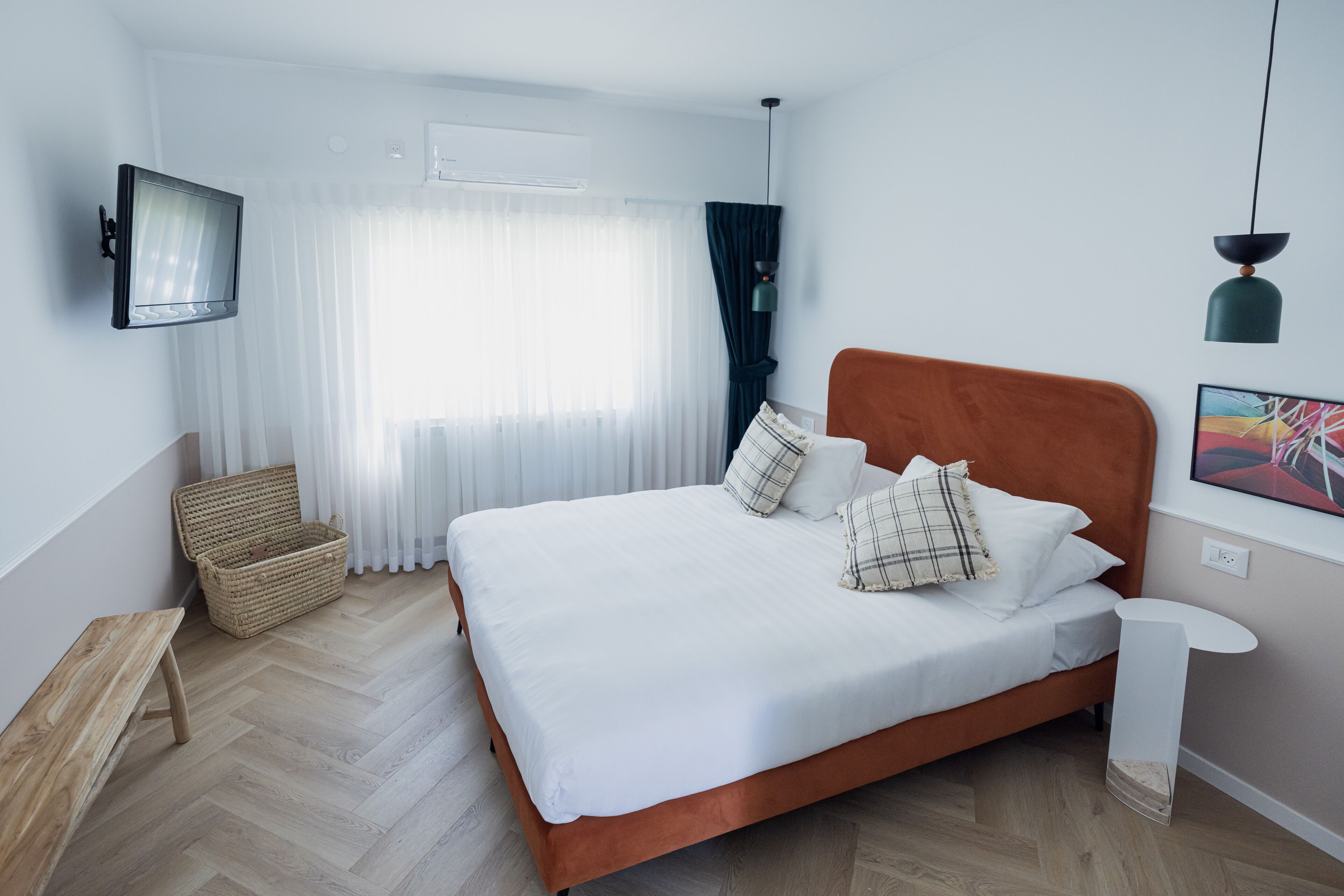 Une chambre à coucher moderne avec un grand lit, un banc, un panier en osier et une petite table.