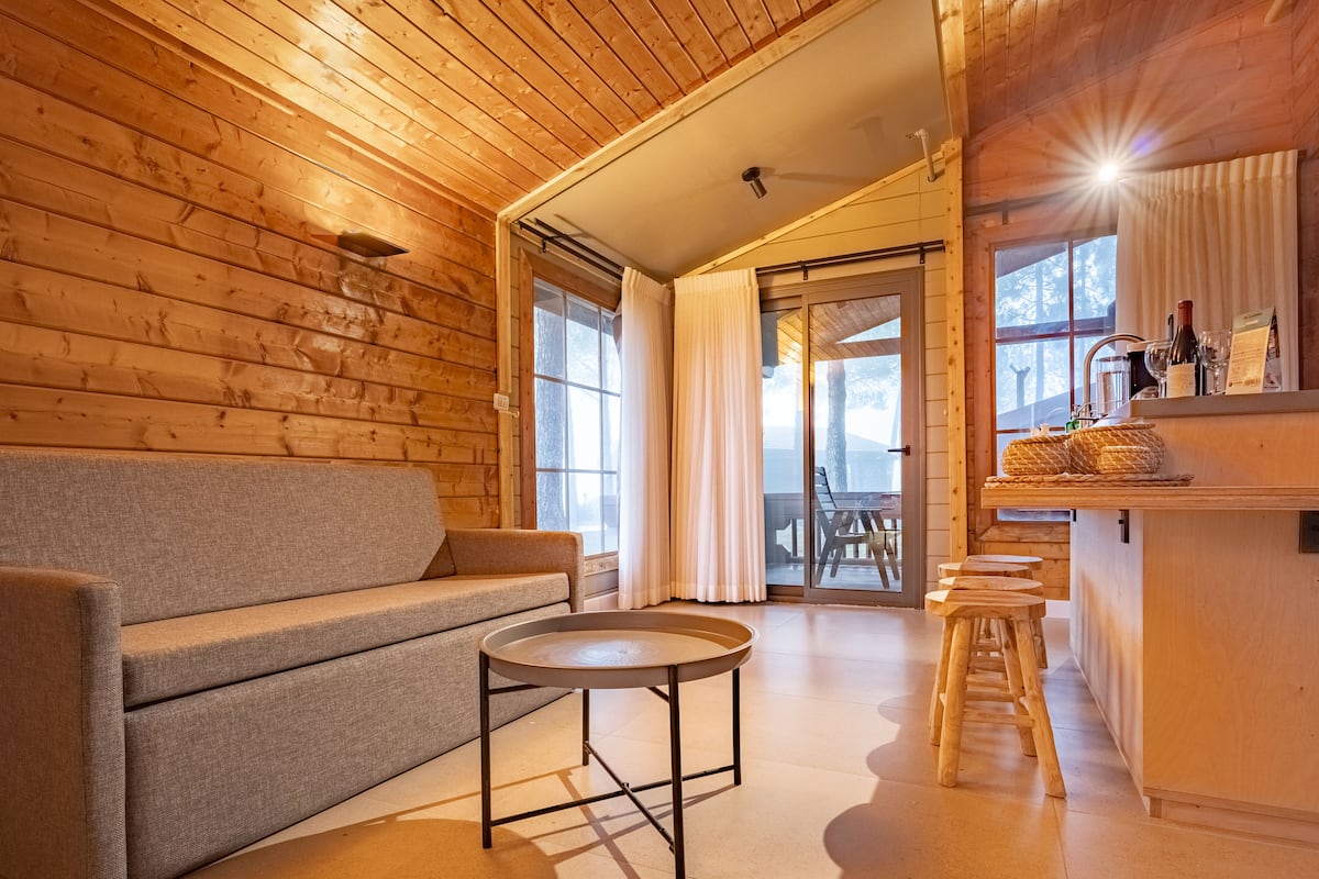 Een knus houten interieur met een bank, een ronde tafel en een bar met krukken.