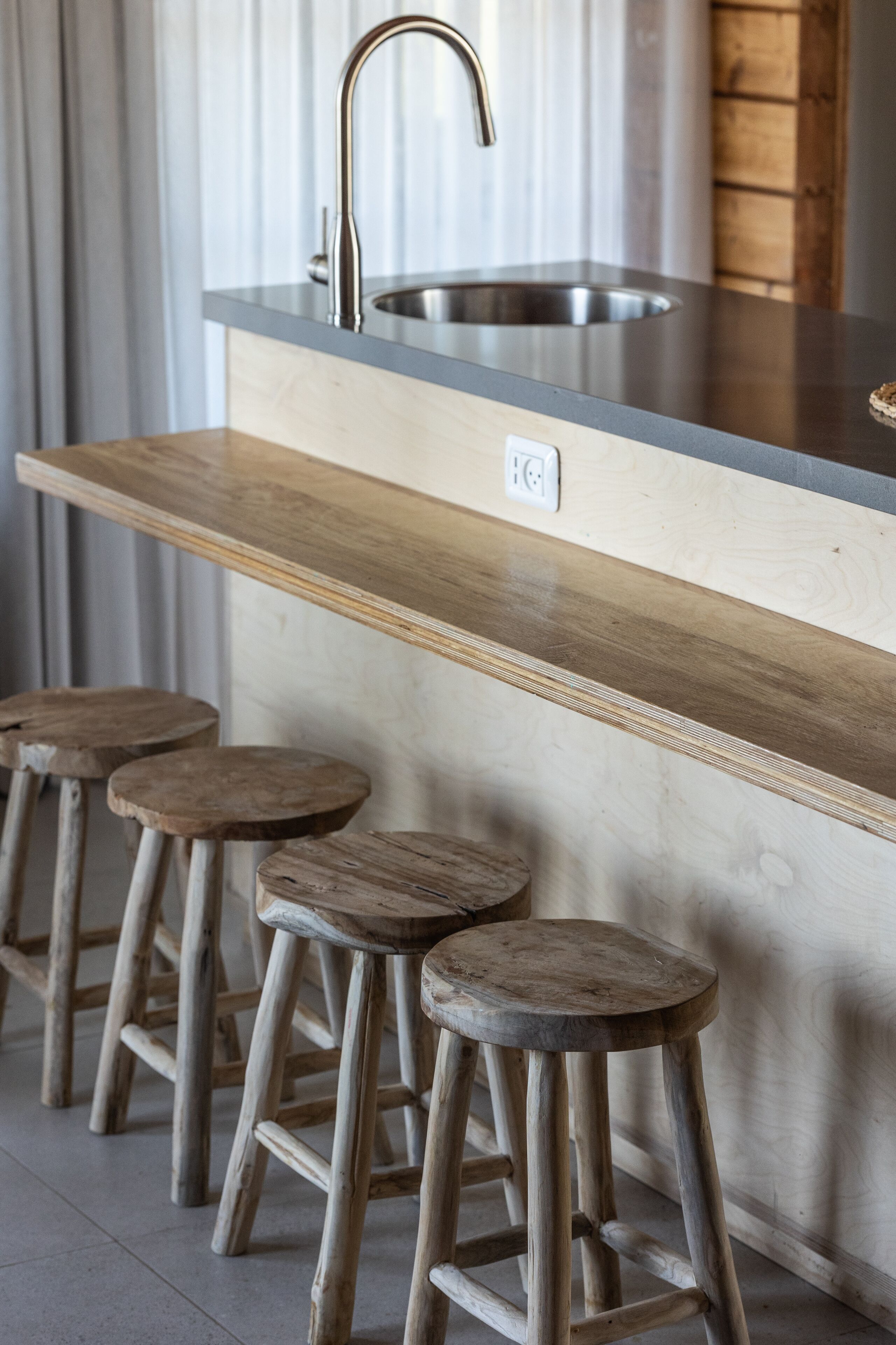 A kitchen with a stainless steel sink, wooden countertop, and three wooden stools.