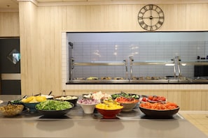 Uma área de buffet com diversas opções de comida e um relógio na parede.