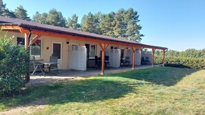 Un espacio de estar al aire libre cubierto, con mesas y sillas, rodeado por una estructura de madera y un techo de metal.