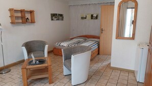 Una habitación pequeña con una cama, una silla, una mesa, un espejo y una estantería.