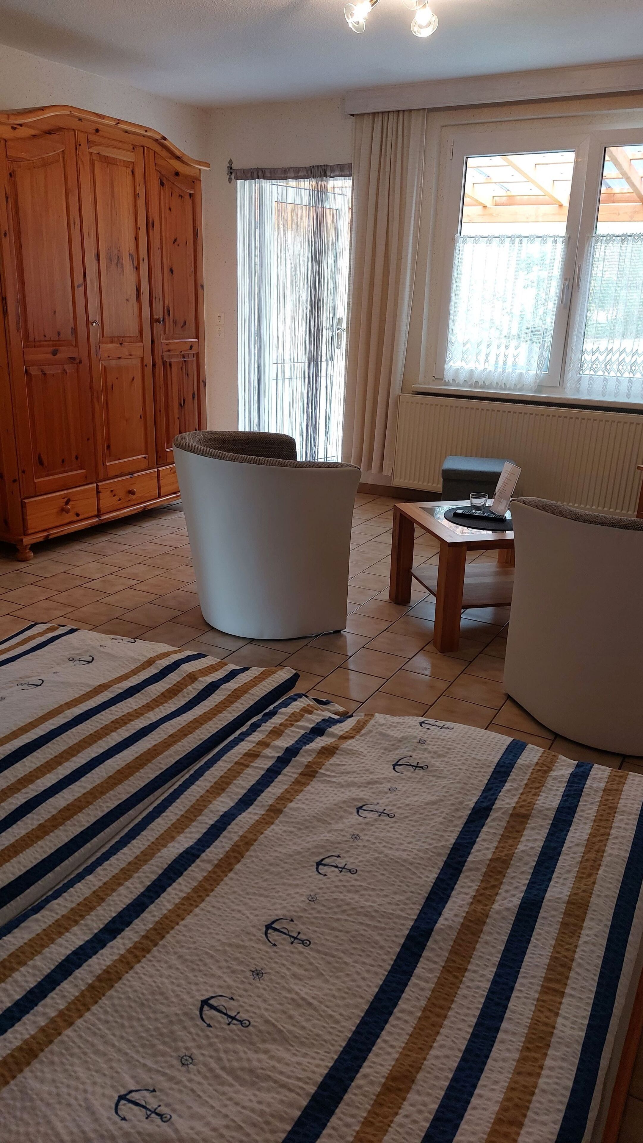 Un salon spacieux comprenant un meuble en bois, un fauteuil blanc, un canapé et une table basse en verre.