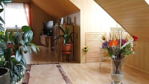 A modern living room with a wooden sloped ceiling, a TV, a potted plant, and a vase of flowers. - Apartment in Starsow (21456) (Mirow)