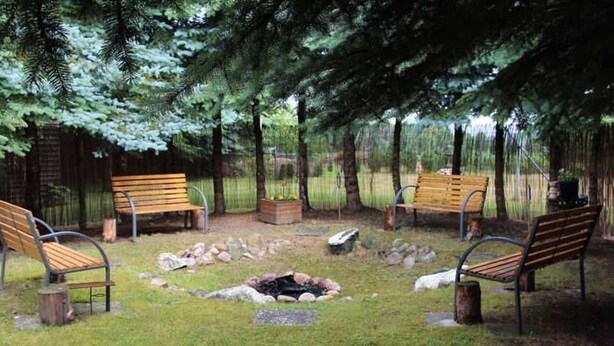 A serene outdoor seating area with wooden benches and a fire pit surrounded by rocks and grass. - Apartment in Starsow (21456) (Mirow)