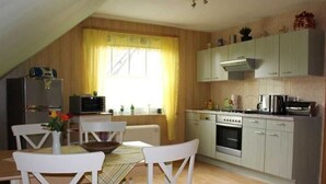 A kitchen with white cabinets, a dining table with chairs, and a window with curtains. - Apartment in Starsow (21456) (Mirow)