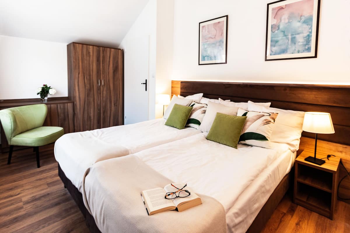 Ein Hotelzimmer mit zwei Betten, einem grünen Sessel, einem Holzschrank und Bildern an der Wand.