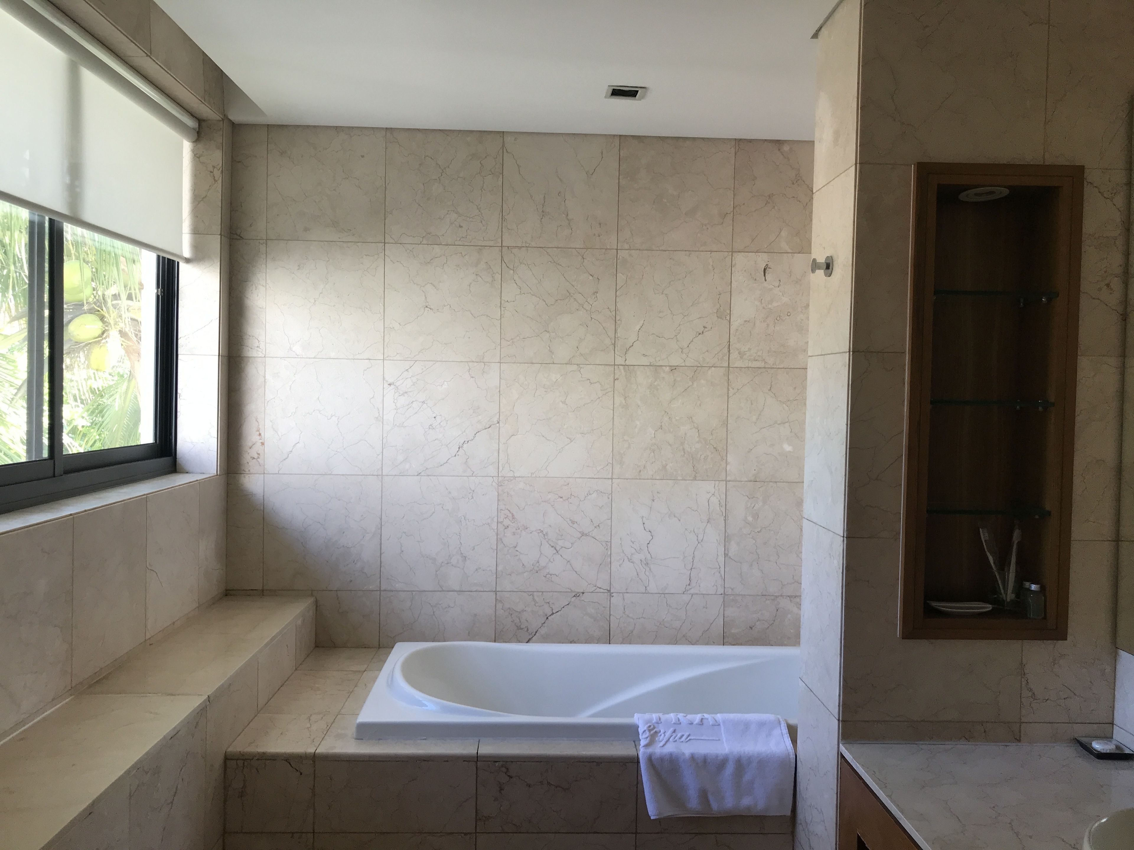 A modern bathroom with a freestanding bathtub, a window with a view of greenery, and a wooden cabinet with a mirror.