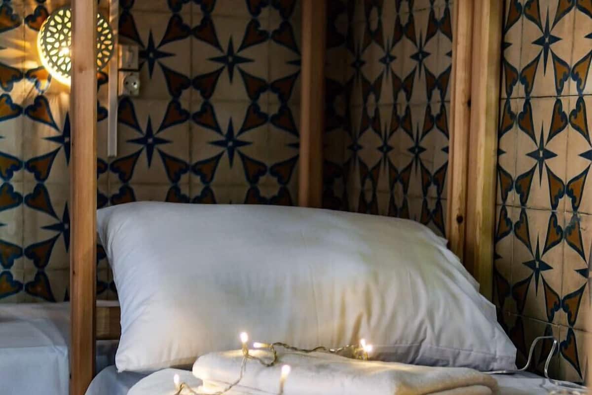 A single bed with white bedding and string lights, wooden frame, and patterned wall tiles.
