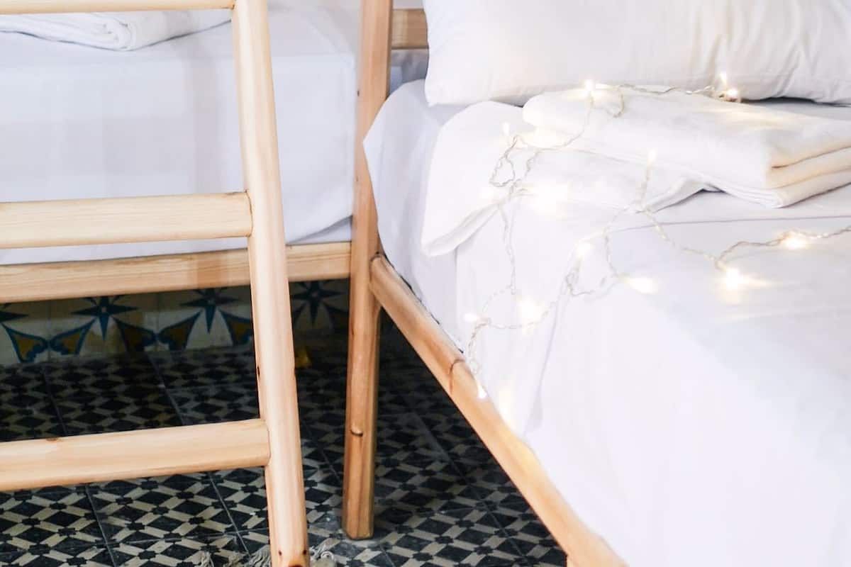 A bunk bed with white bedding and a wooden ladder. The room has patterned tile walls and a checkered floor.