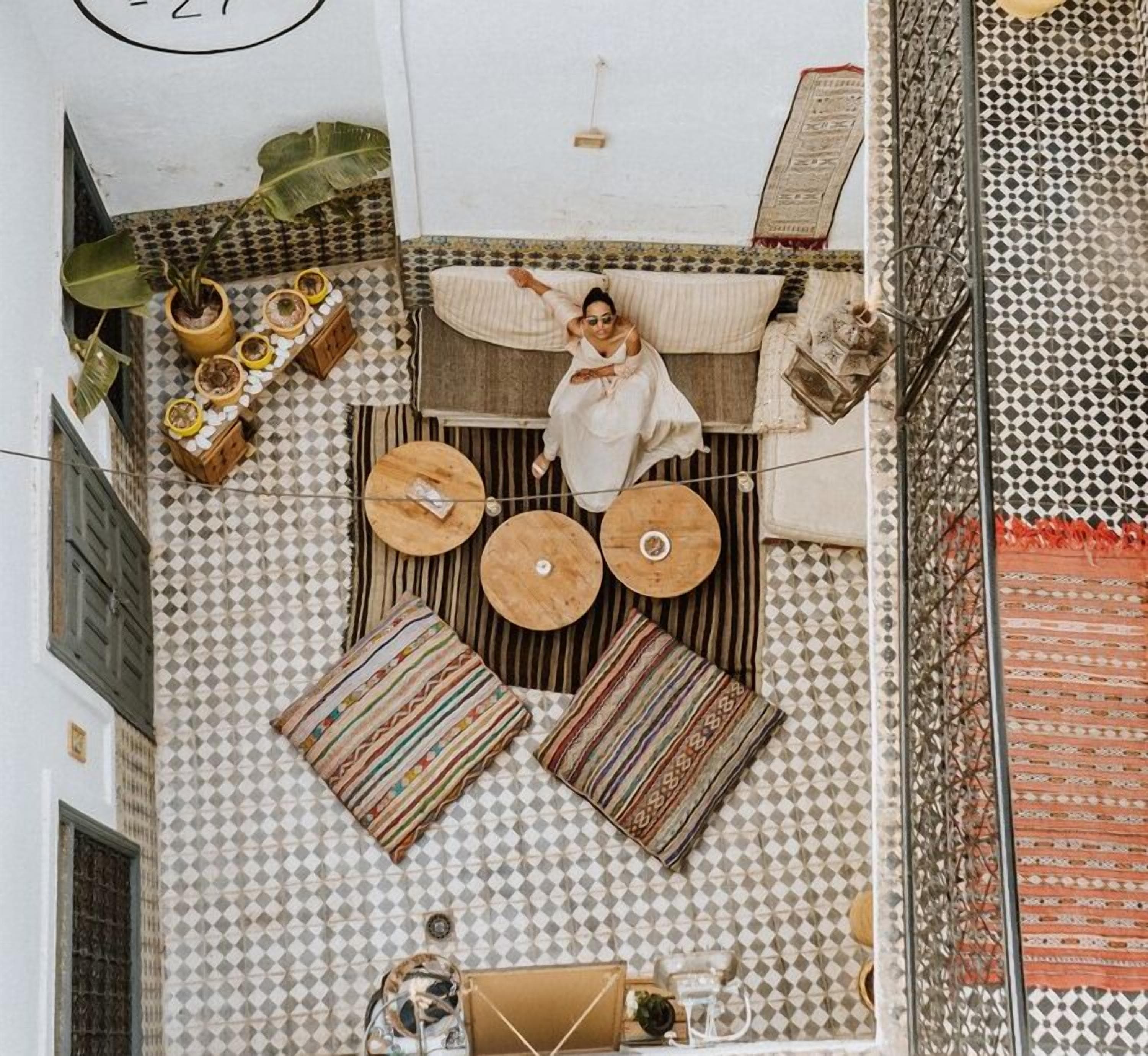 A high-ceilinged room with a checkered floor, a central seating area with a sofa and two round tables, and a hanging plant.