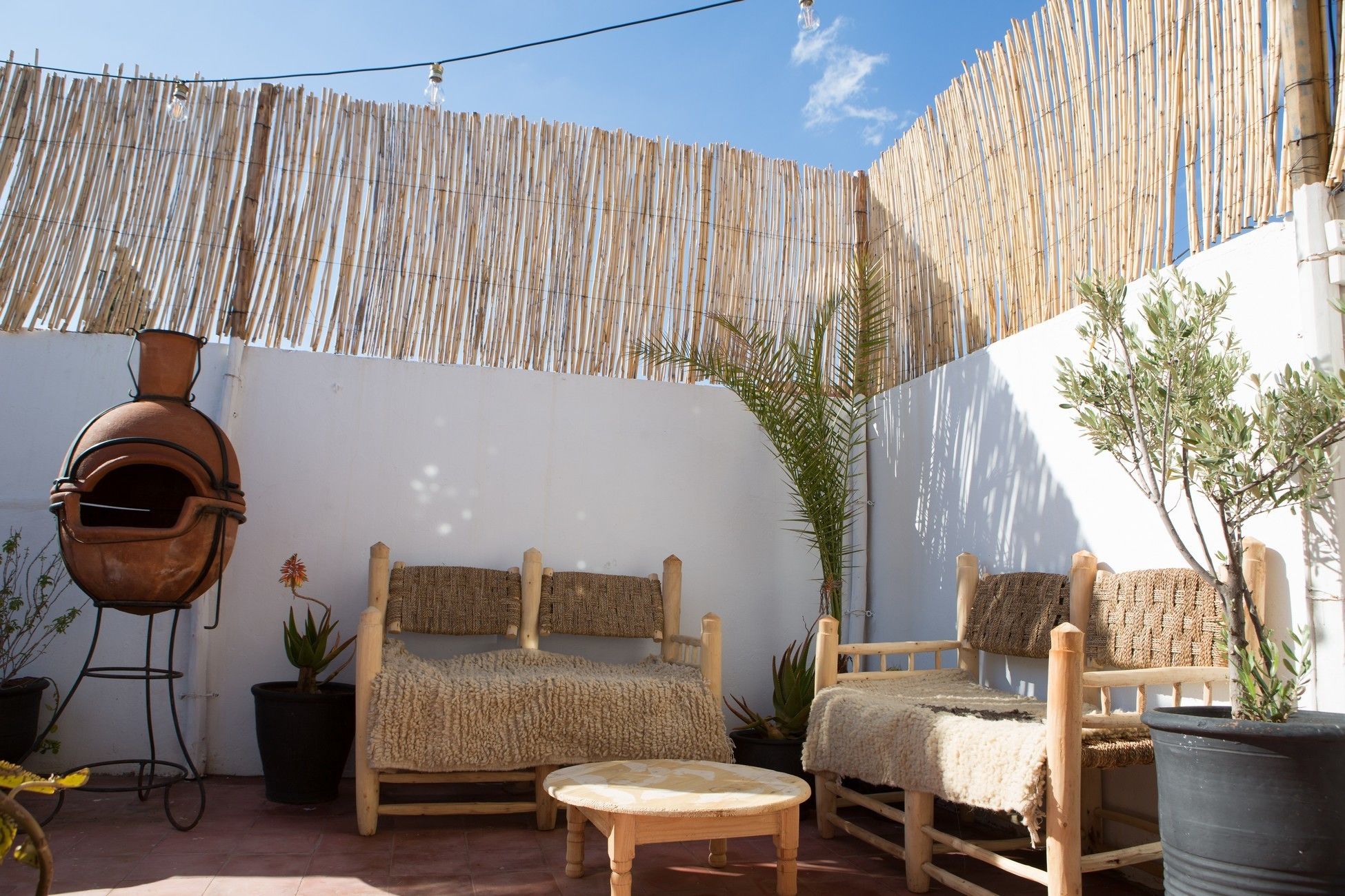 Un patio exterior con un área de estar rústica, un horno de barro y plantas en macetas.