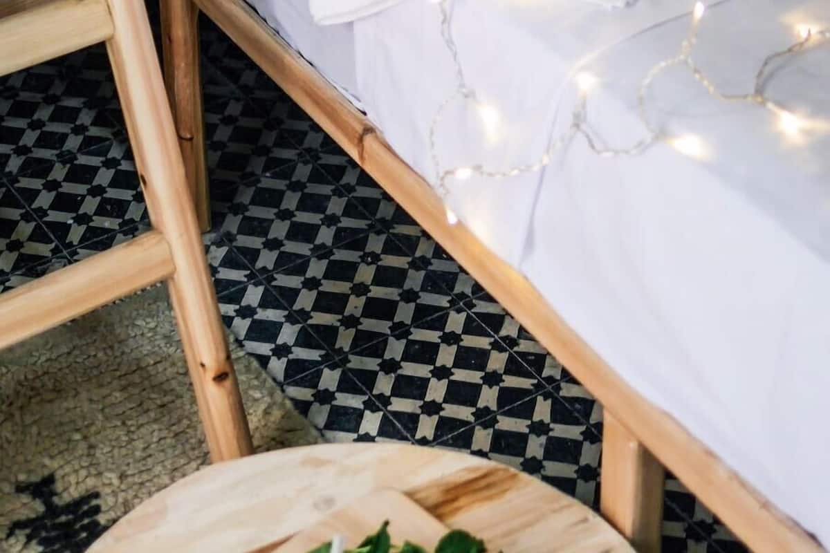 A bunk bed with white bedding and string lights, a round wooden table with a glass of water and a lemon, and a patterned floor.