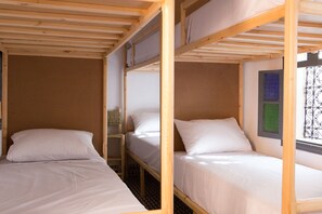 Ein Zimmer mit drei Etagenbetten, Holzbalken und einem Fenster mit schmiedeeisernen Gitterstäben.
